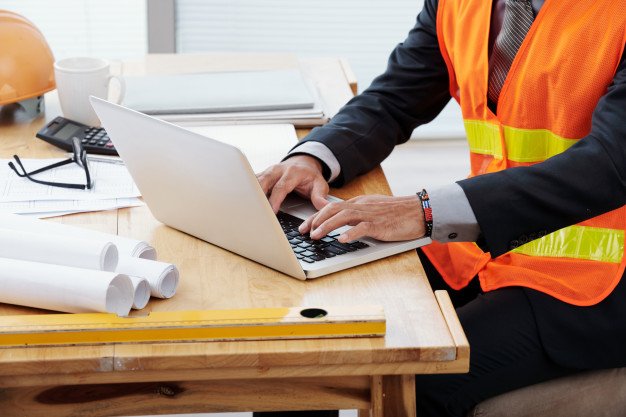 hombre-irreconocible-neon-chaleco-seguridad-traje-negocios-sentado-escritorio-usando-laptop_1098-17504